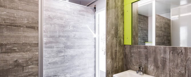 Moderner Waschraum mit Holzoptik, Waschtisch und grünem Spiegelrahmen, gut beleuchtet durch Oberlicht.