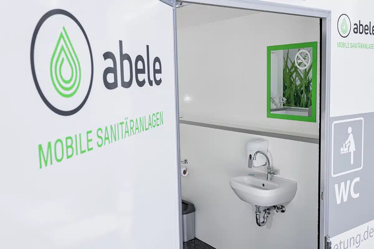 Toilettencontainer Handicap 8 Mobile Sanitäranlage von Abele mit Waschbecken, Seifenspender und Spiegel, darauf Hinweis auf Rauchverbot.