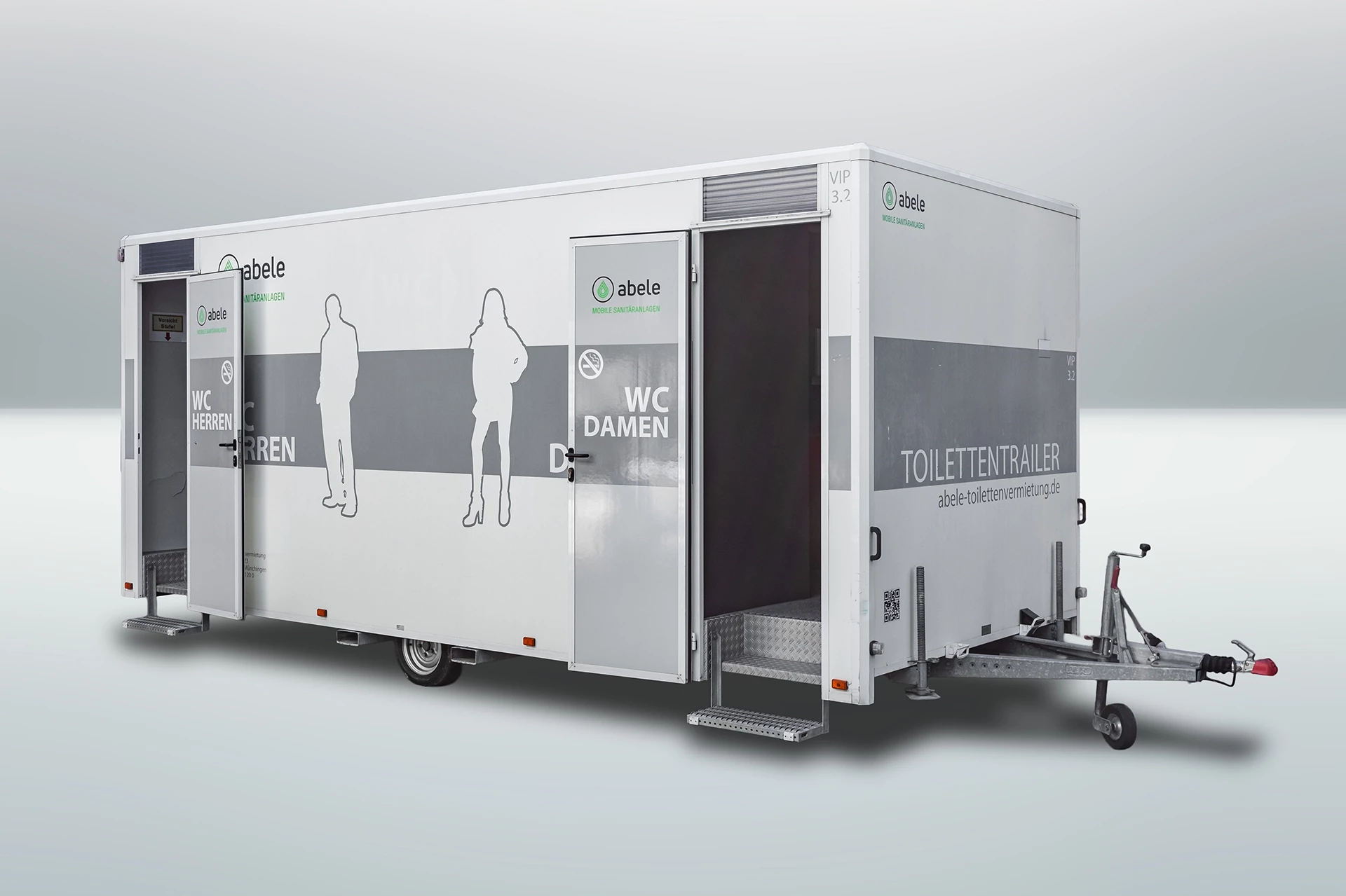 Toilettenwagen Modell Exklusiv – Mix 3/2 5 Moderner mobiler Toilettenanhänger mit separaten Eingängen für Damen und Herren, abgestellt auf hellem Untergrund.