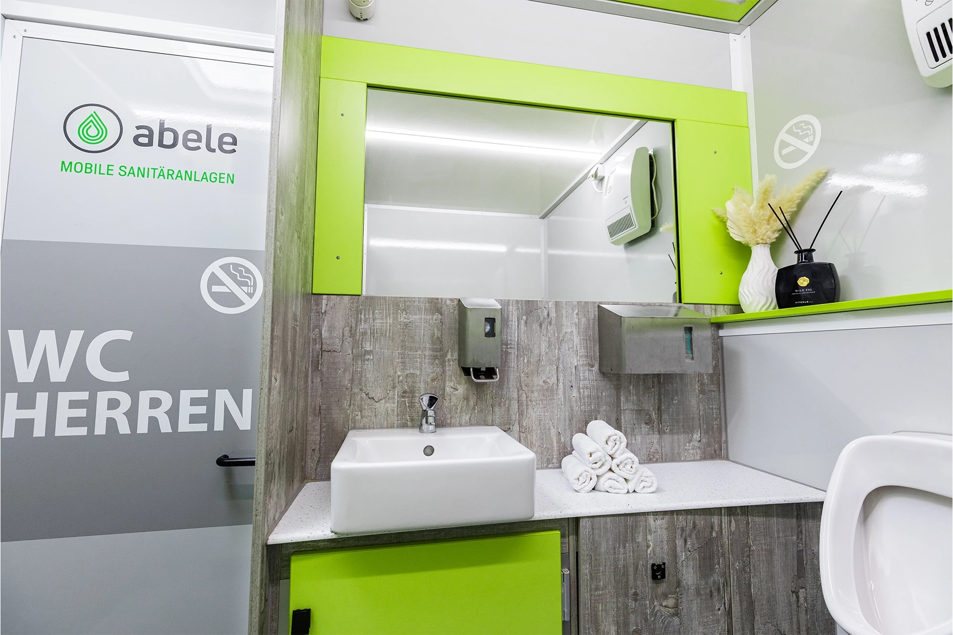 Luxus Toilettenwagen Modell Exklusiv – GoGreen 9 Modernes mobiles Herren-WC mit Waschbecken, Spiegel, Handtuchhalter, Seifenspender, Dekoration und Verbotsschild gegen Rauchen.