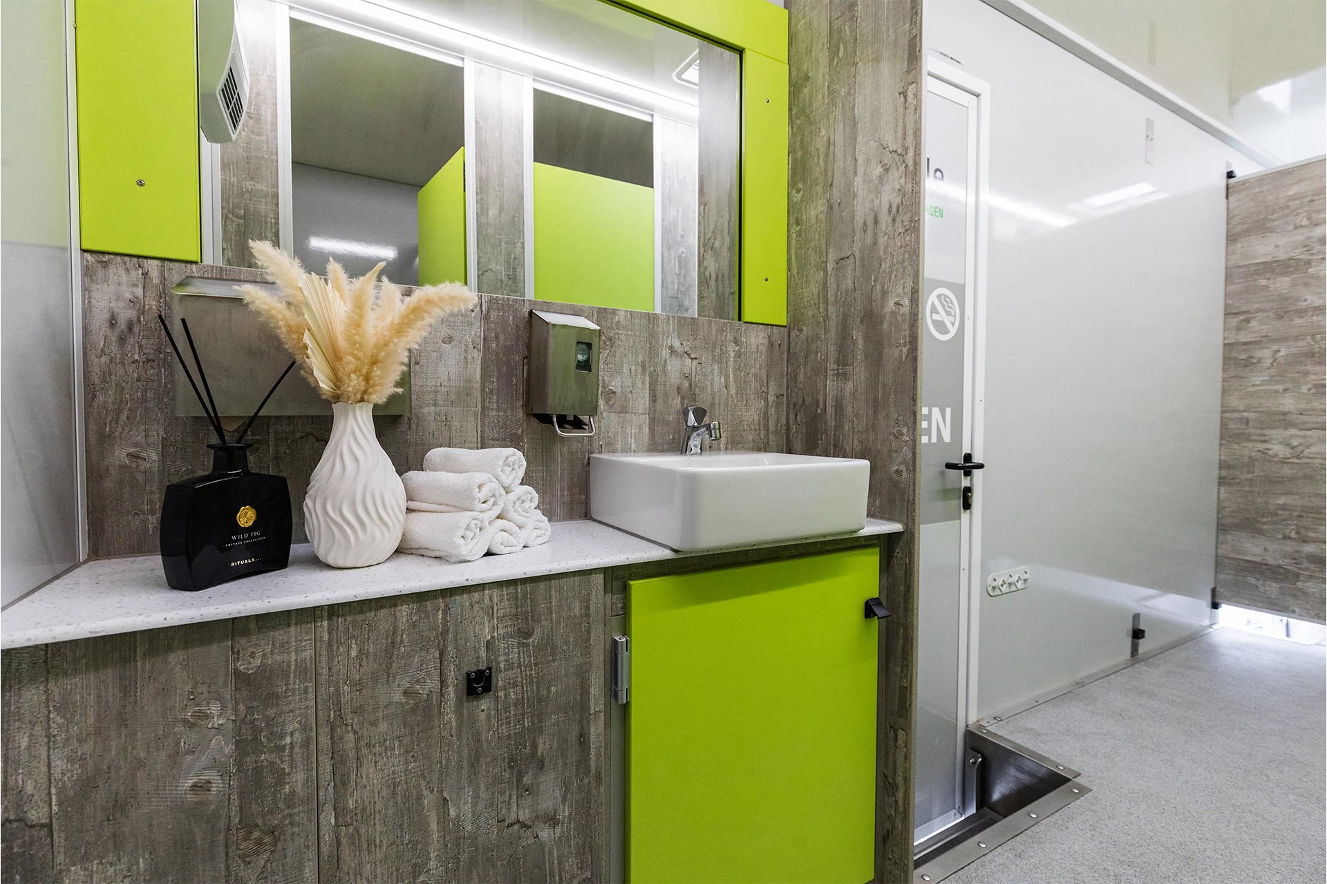 Luxus Toilettenwagen Modell Exklusiv – GoGreen 5 Moderner Waschtisch mit grünem Schrank, Waschbecken, Handtüchern und Deko in einem stilvollen Badezimmer.