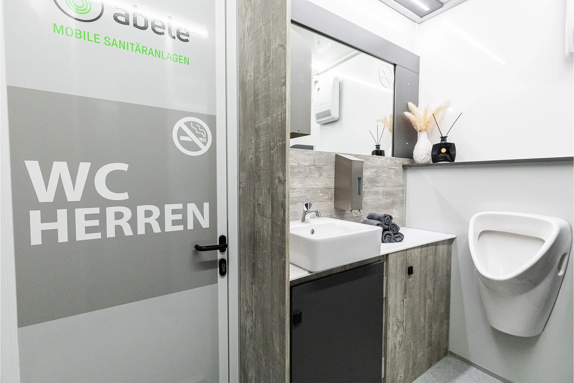 Toilettenwagen Modell Exklusiv – GoGrey 7 Herren-WC mit moderner Einrichtung, inkl. Waschbecken, Pissoir und Deko. Hinweis: Rauchen verboten. Türen mit Beschriftung.