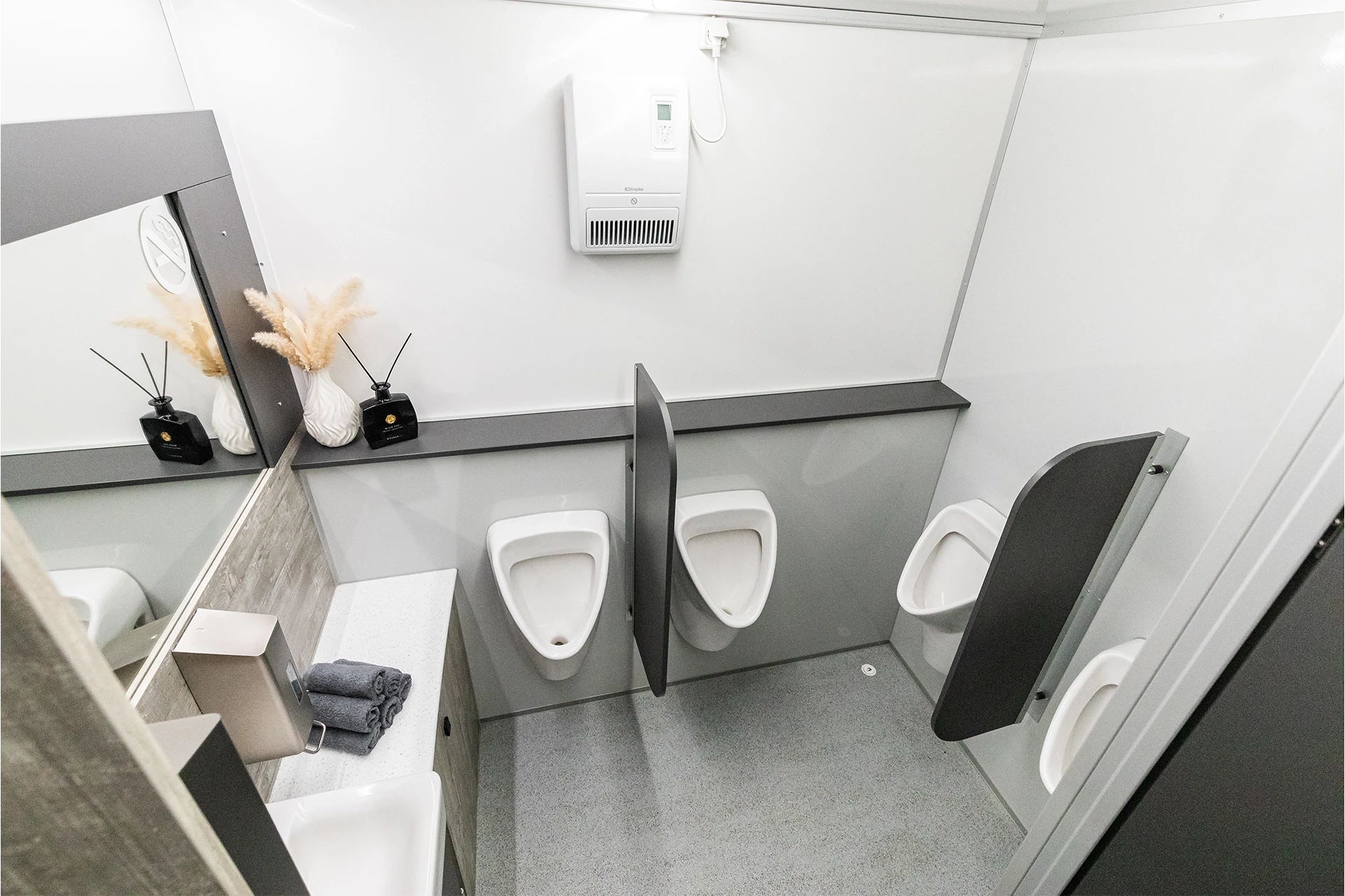 Toilettenwagen Modell Exklusiv – GoGrey 6 Moderne Herrentoilette mit drei Urinalen, Waschbecken, Spiegel, Handtücher, Raumduft und Pflanzen zur Dekoration.