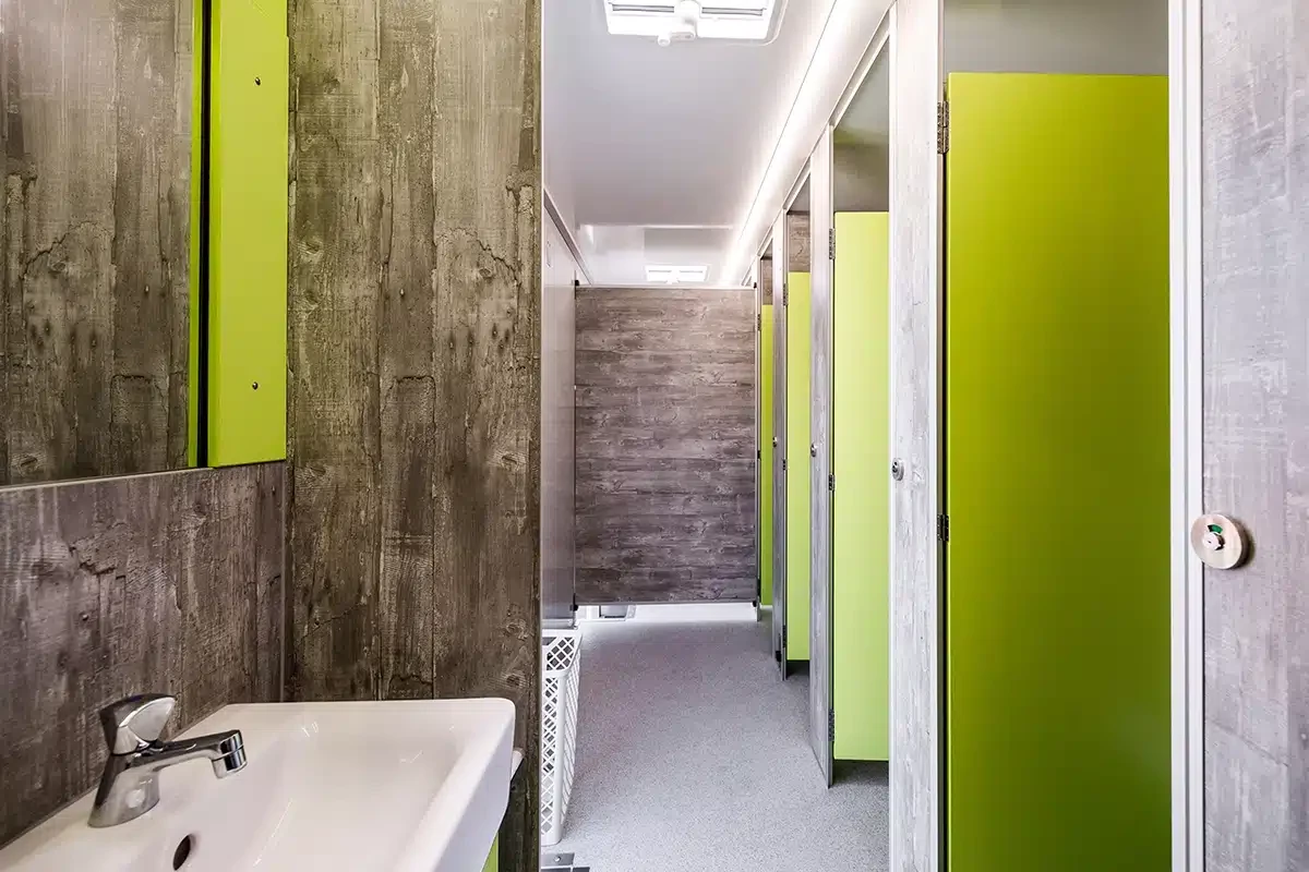 Toilettenvermietung Stuttgart 11 Moderne öffentliche Toilette mit grauen und grünen Kabinen, Waschtisch links, gut beleuchtet.