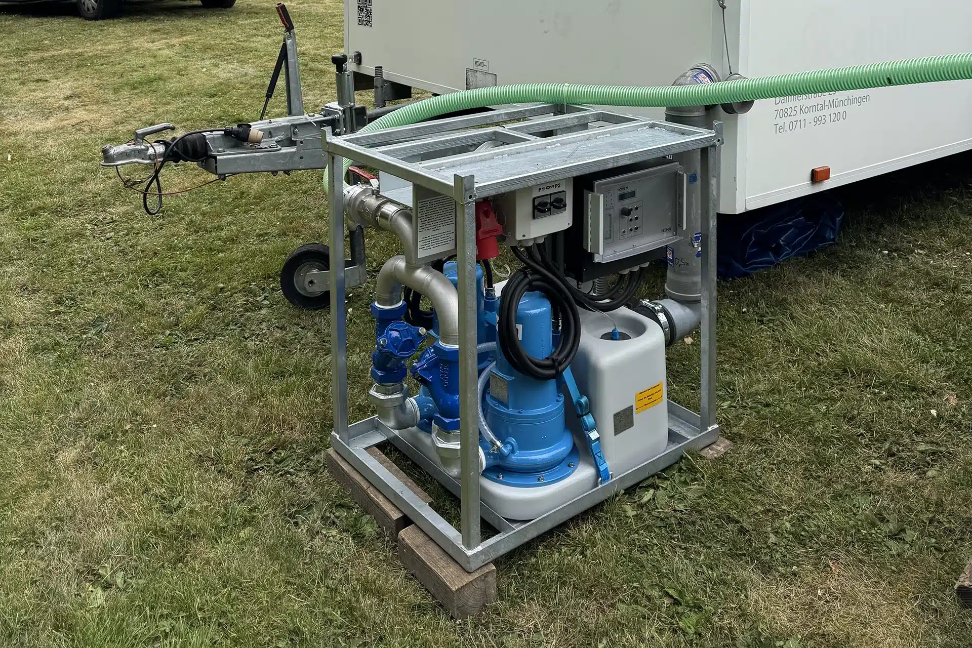 Abwassertank / Pumpe 11 Mobilstation zur Wasserförderung mit blauen Rohren und Pumpe, aufgebaut auf einer Holzplattform im Grünen.